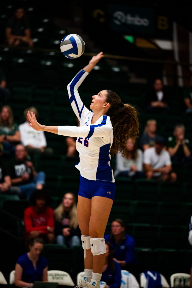 A volleyball player in white and blue spikes a volleyball.