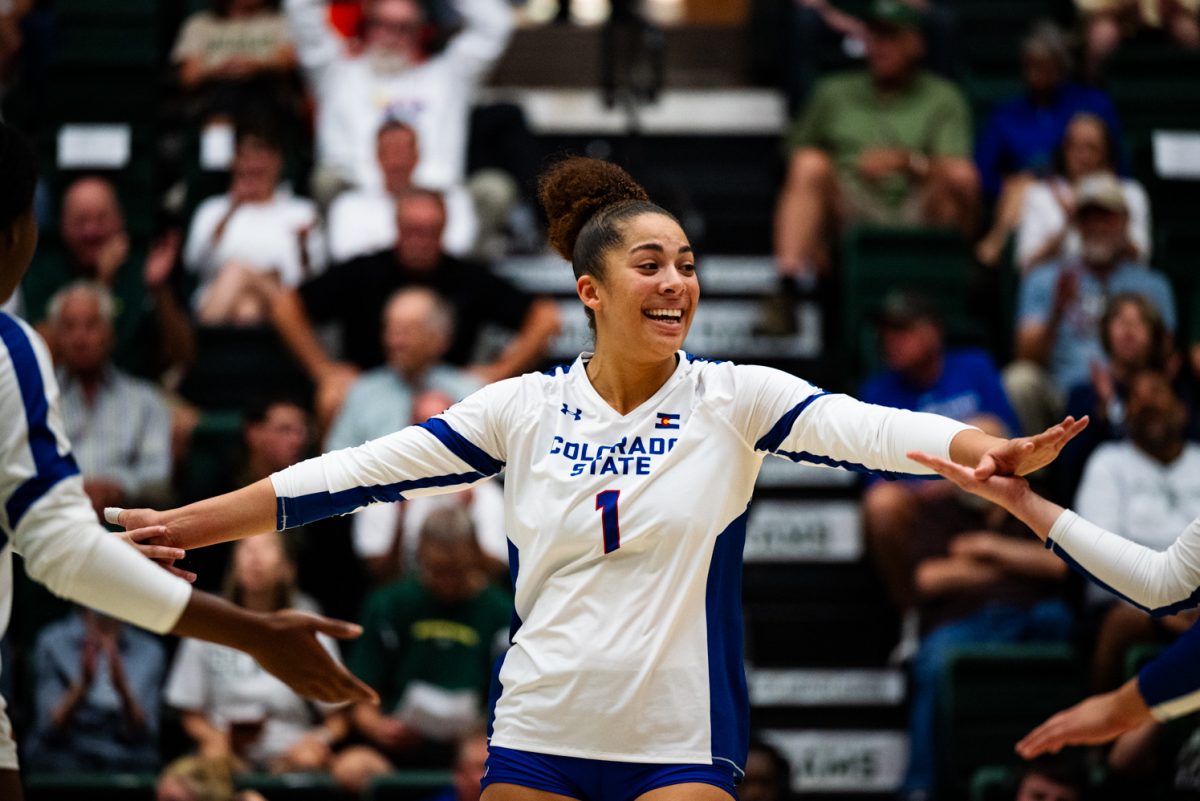 A volleyball player in white and blue smiles with her hands outstretched to high five other players.