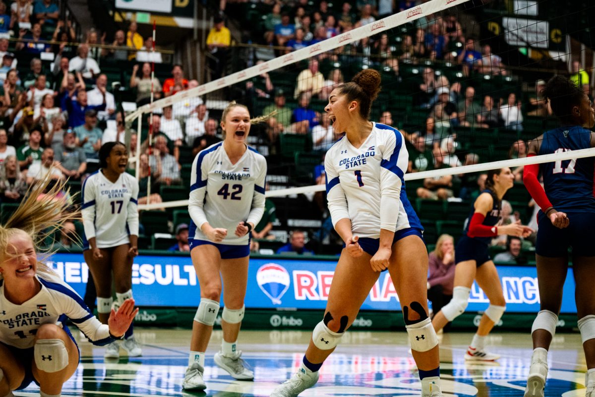 Four volleyball players in white and blue yelling in celebration.