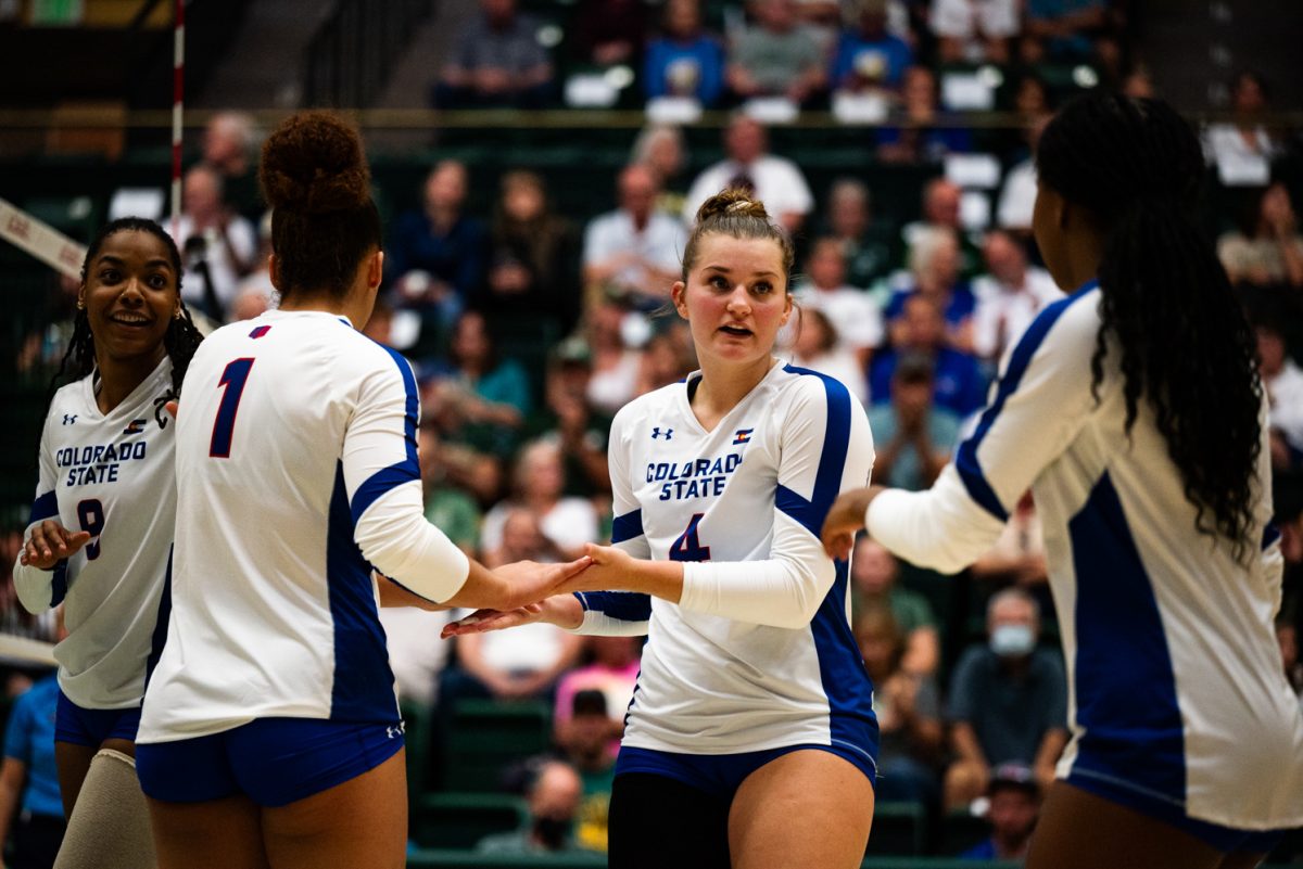 Volleyball players in white and blue high five each other.