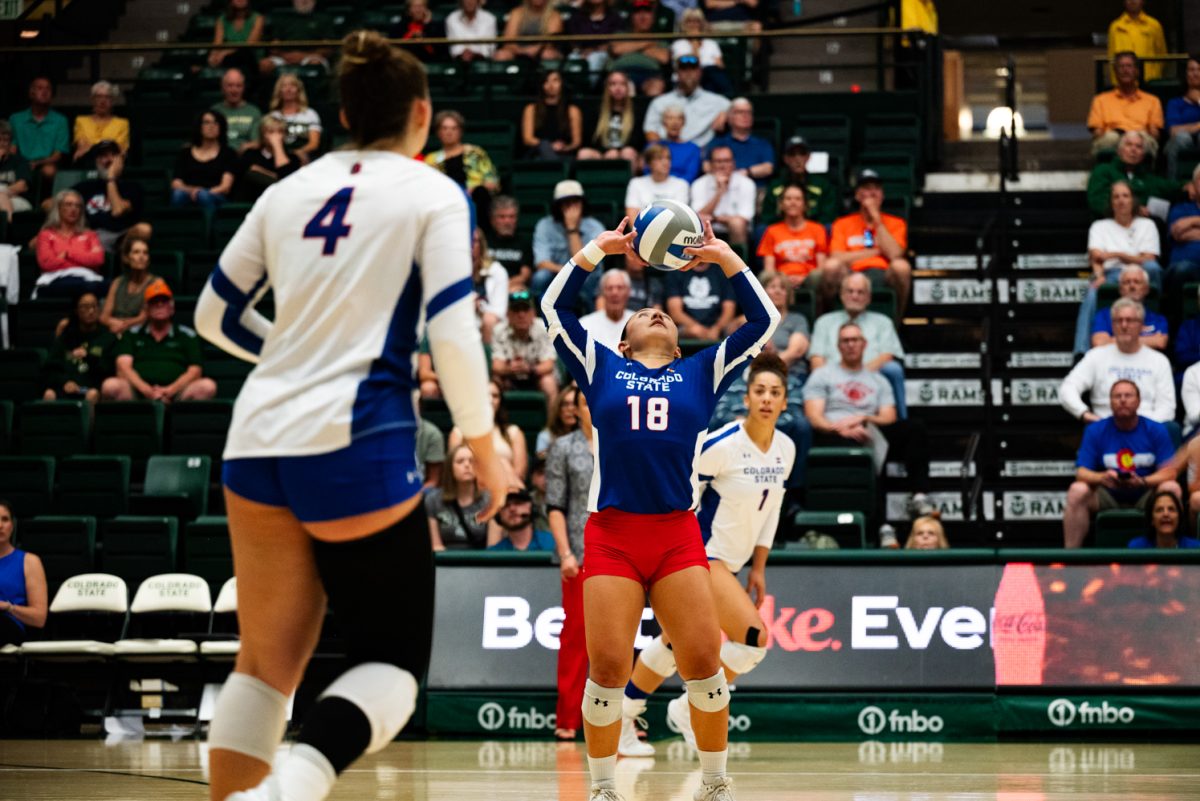 A volleyball player in blue, white and red leans back and sets a volleyball.