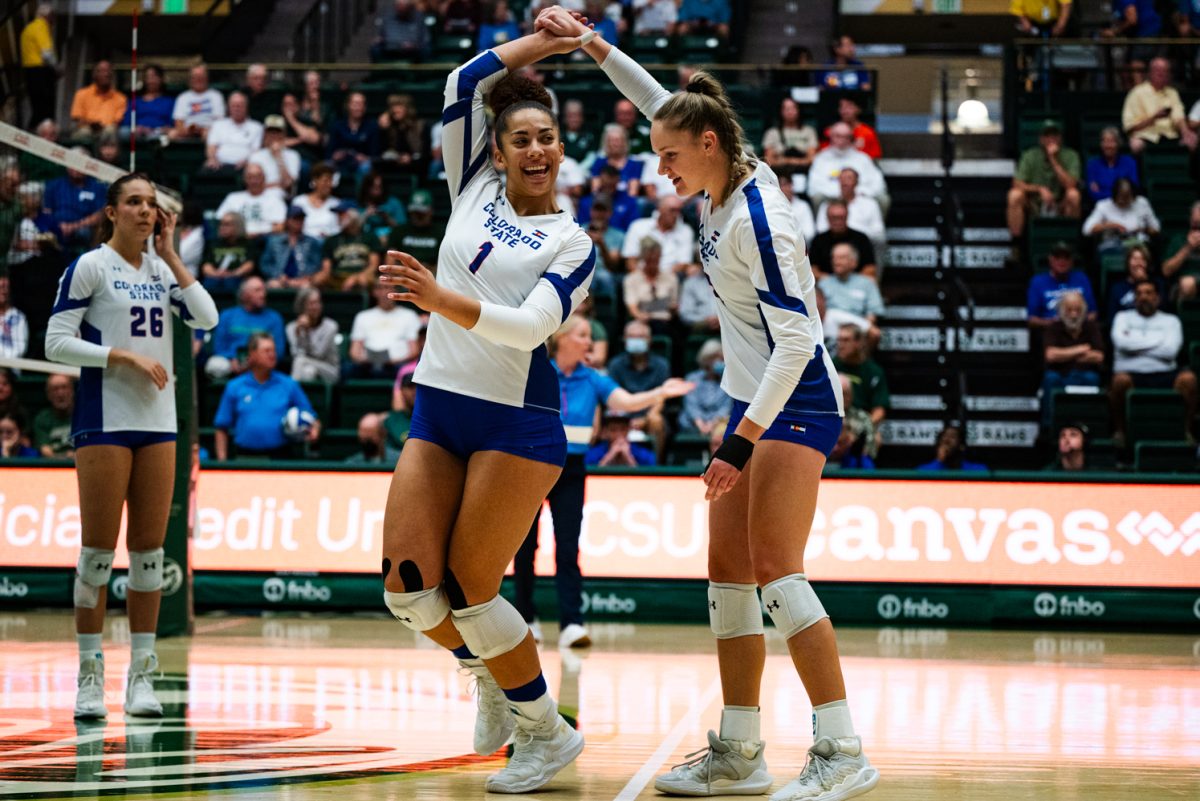 A volleyball player in white and blue twirls a second volleyball player in white and blue.