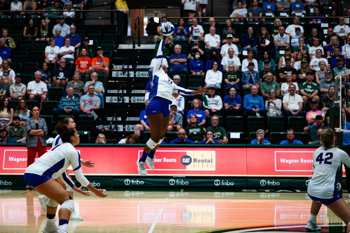 A volleyball player in white and blue jumps up to hit a volleyball.