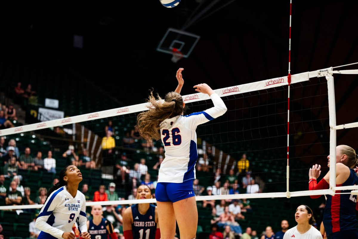 A volleyball player in white and blue lands after jumping to hit a volleyball.