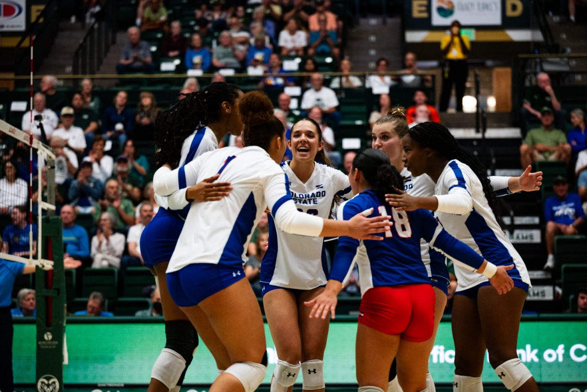 Volleyball players in white and blue huddle together and cheer.