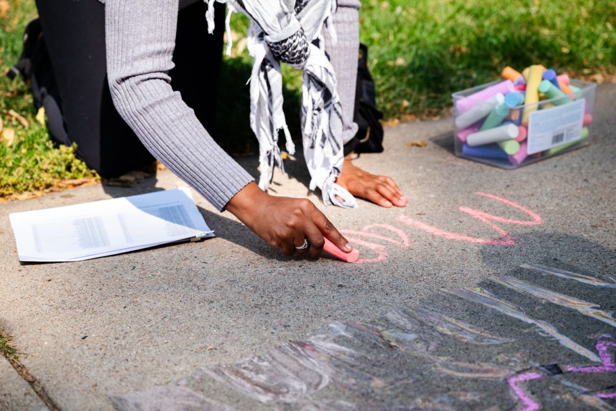 A person on their hands and knees writing in pink chalk.