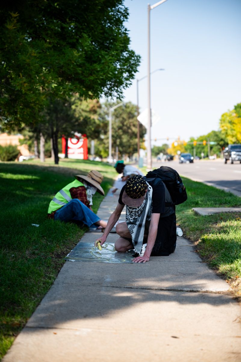 Two people sit on a sidewalk drawing with chalk.