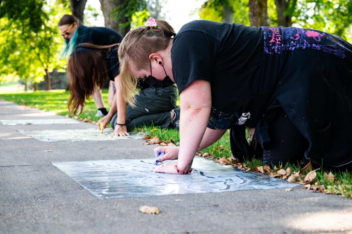 Three people trace templates in chalk.