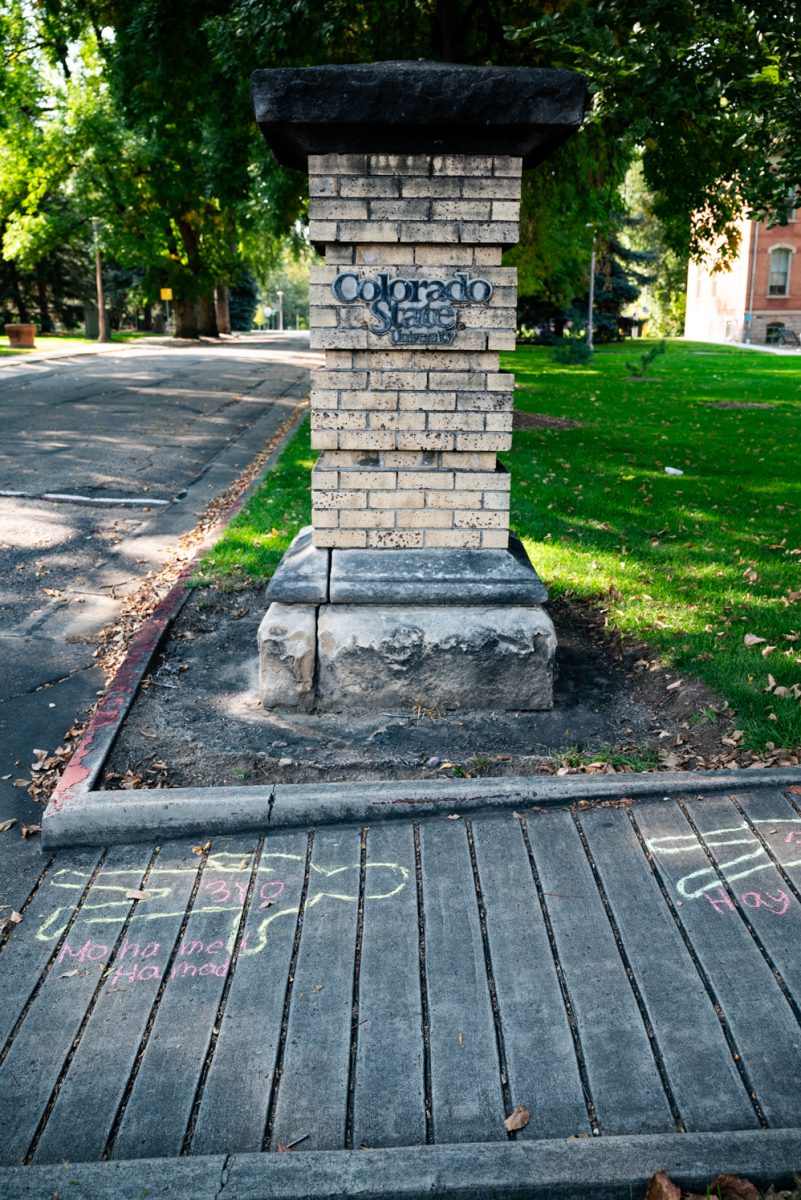 A pillar reading "Colorado State University" with chalk outlines of children on the sidewalk in front of it.