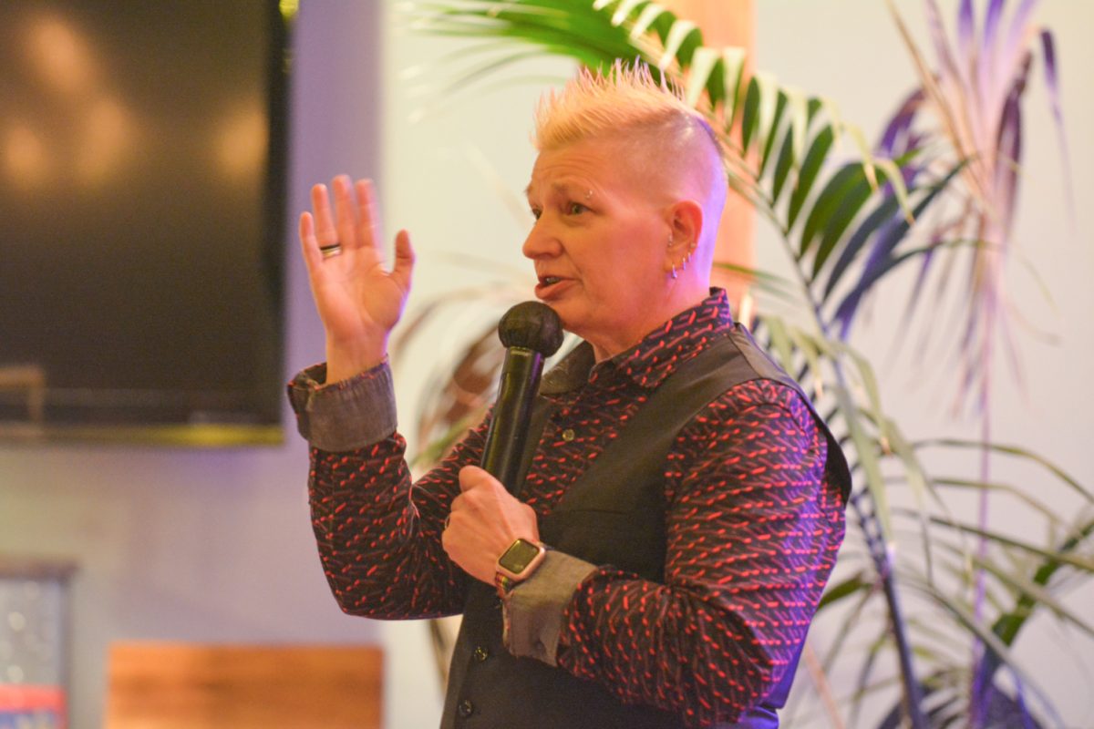 A speaker holding a microphone with her hand raised looking to the crowd