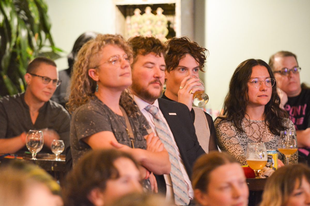 Crowd focusing on comedian, one person is drinking while listening as well.
