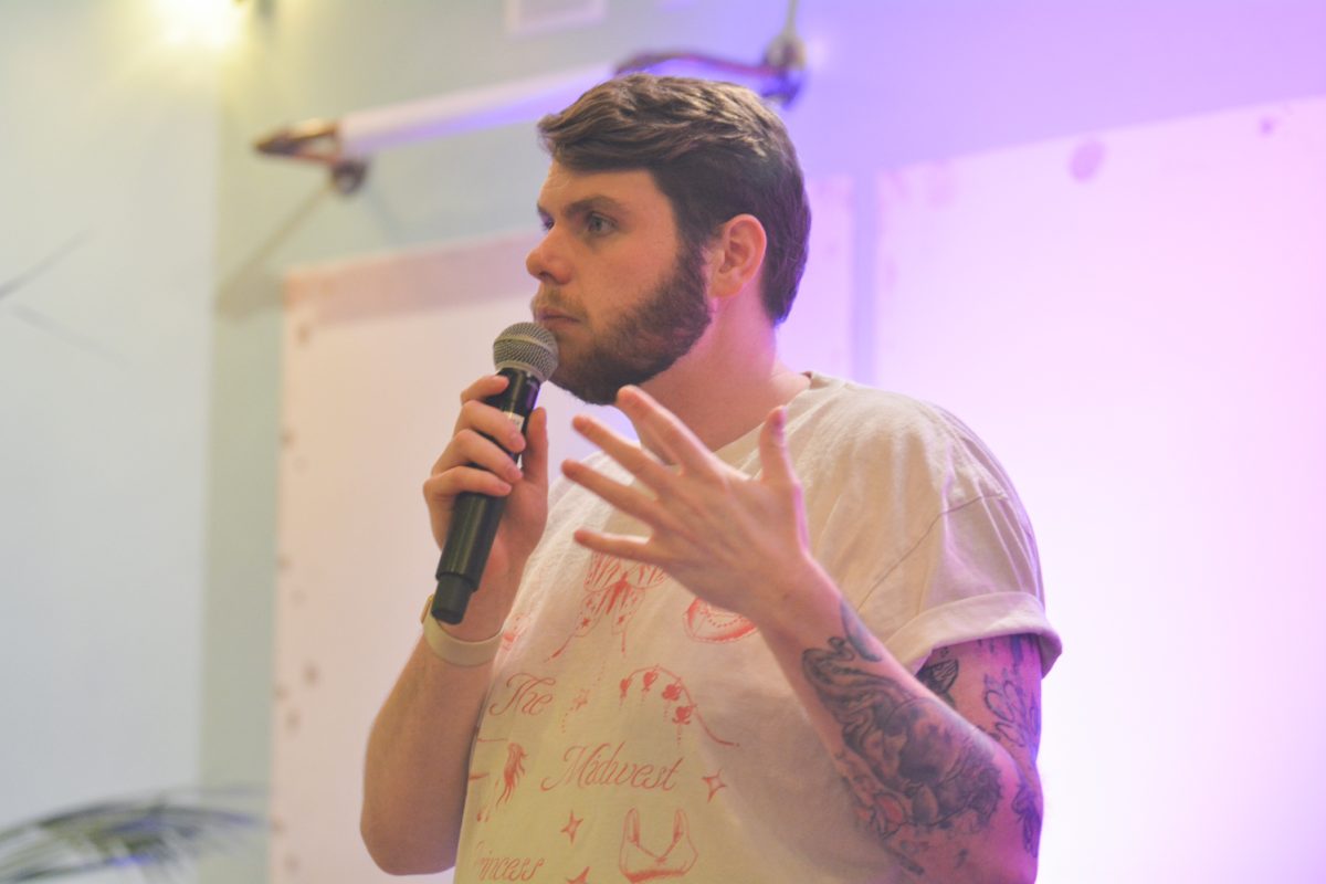 A speaker holding a microphone to his mouth with his hand raised looking out to the crowd.