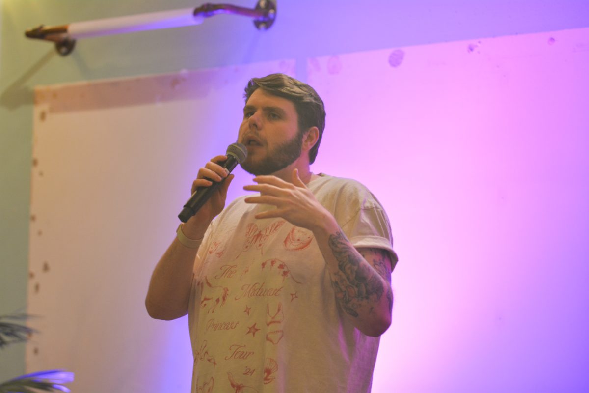 A speaker holding a microphone to his mouth looking to the crowd.