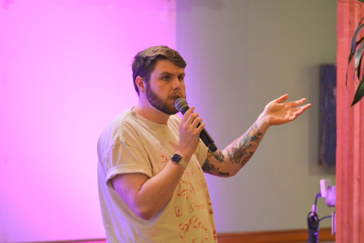 A speaker holding a microphone to his mouth with his hand raised up while looking to the crowd.