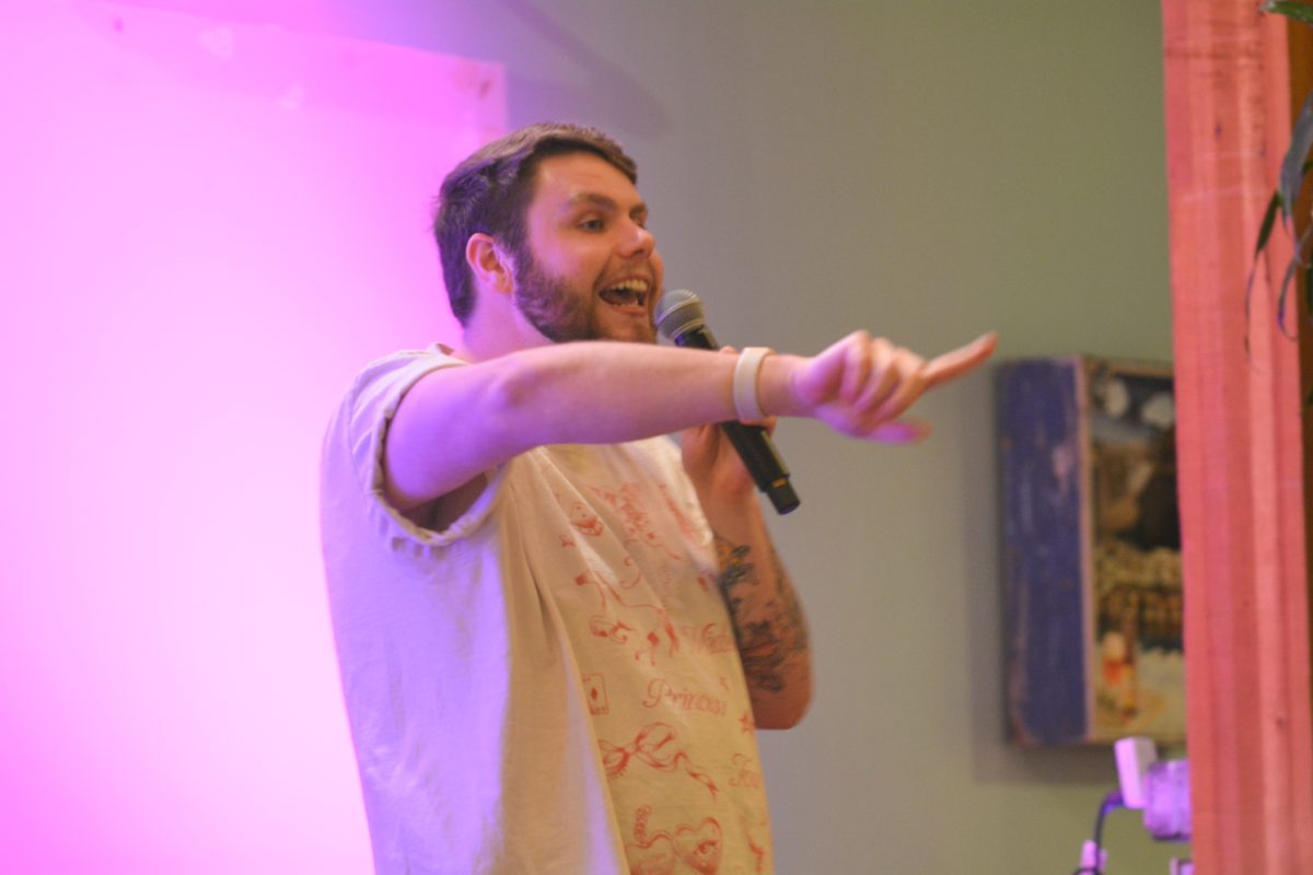 A speaker holding a microphone to his mouth pointing his finger to the crowd.
