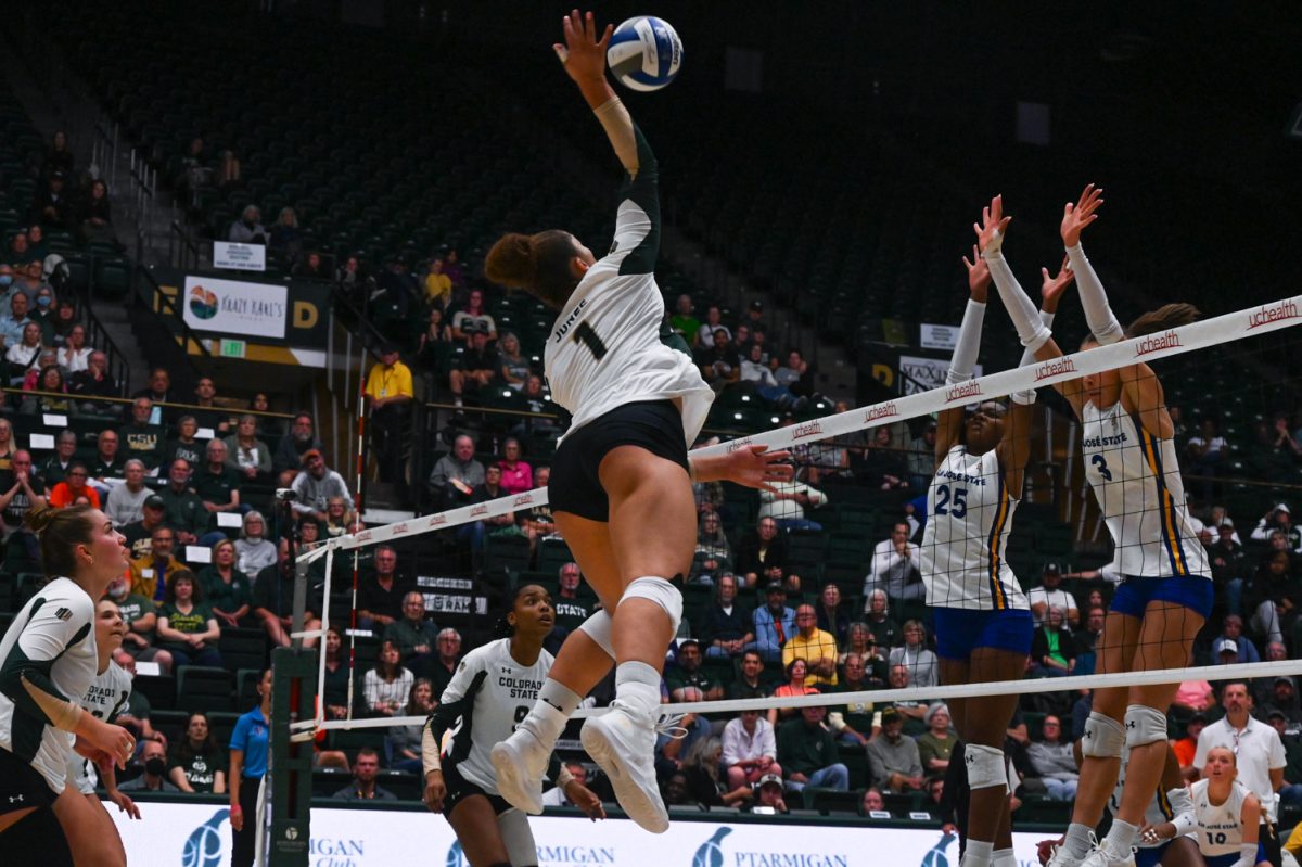 A player in white and green and black shorts hits a blue and white ball on a volleyball court