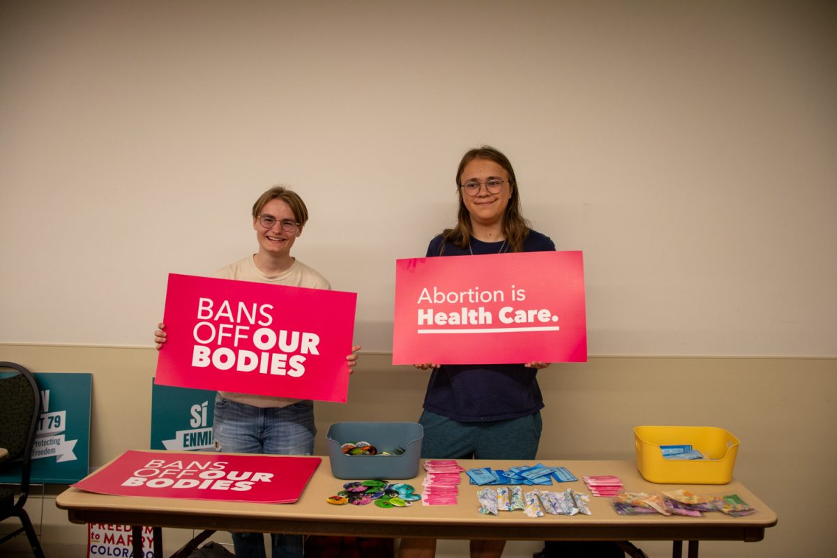 Two people holding signs standing behind a table with things on it.