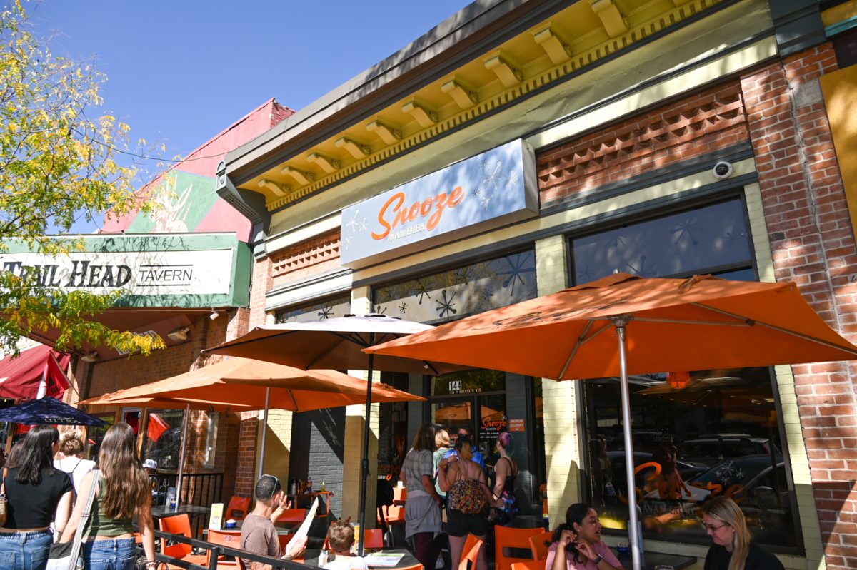 The outside of a restaurant with people outside and orange chairs tables and umbrellas