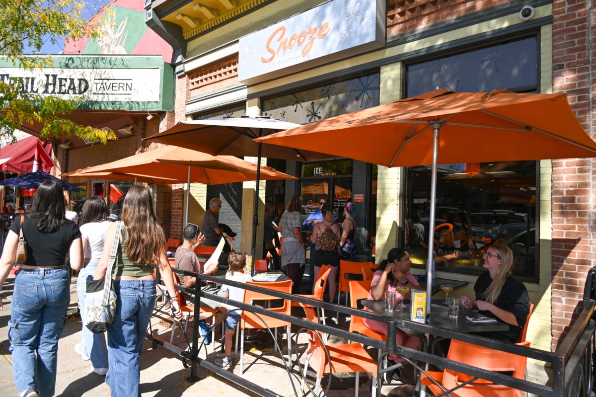 The outside of a restaurant with people outside and orange chairs tables and umbrellas