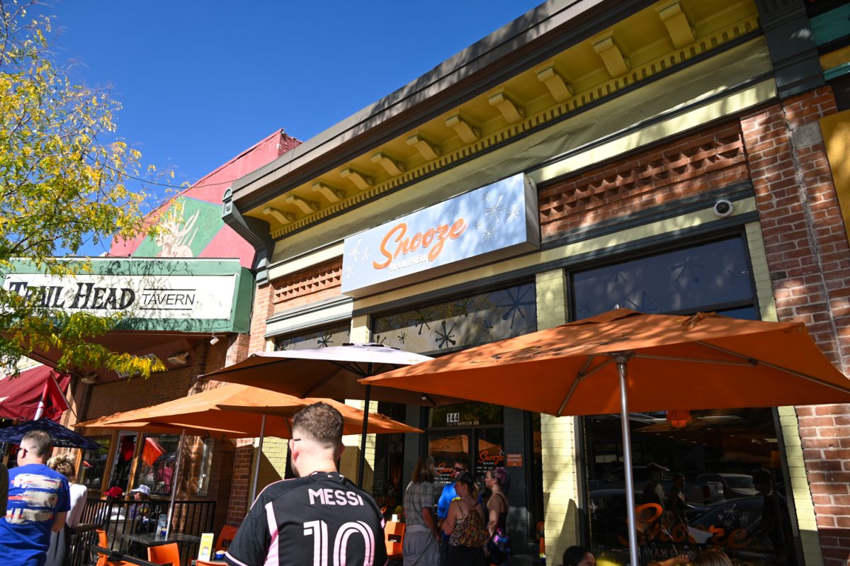 The outside of a restaurant with people outside and orange chairs tables and umbrellas