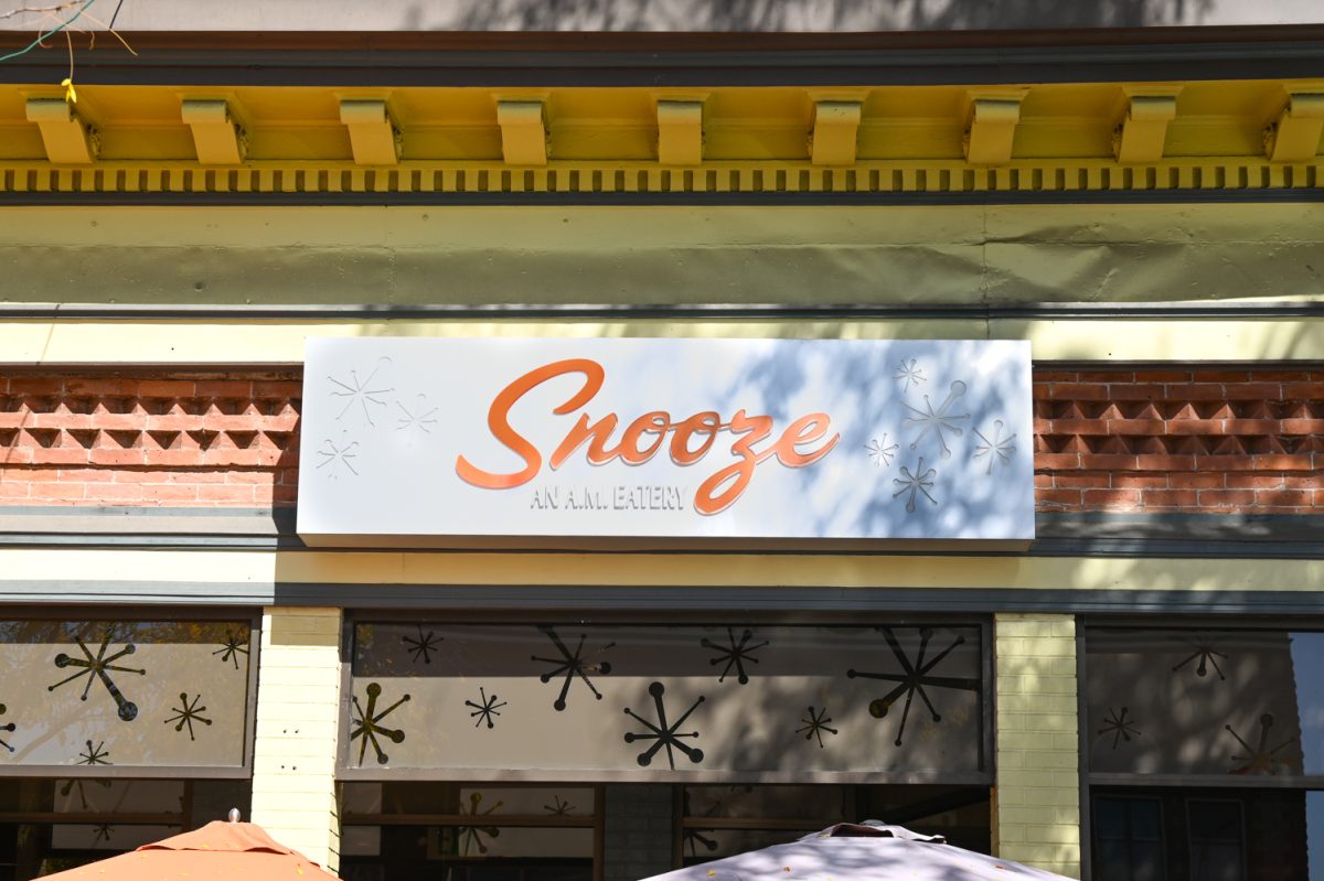 a white and orange sign on a brick building that reads "Snooze"