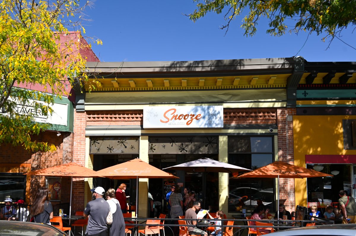 The outside of a restaurant with people outside and orange chairs tables and umbrellas