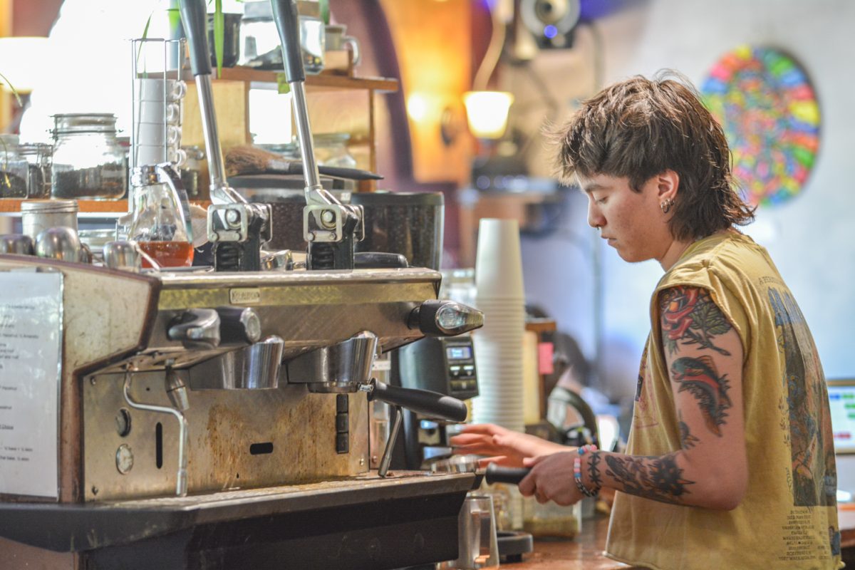 A barista in a yellow tank top making coffee behind a counter.