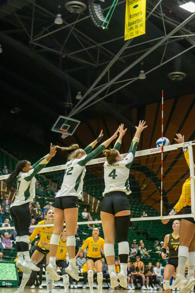 Three female athletes jump at the same time with their arms in the air. Trying to block a ball incoming from the other team's side