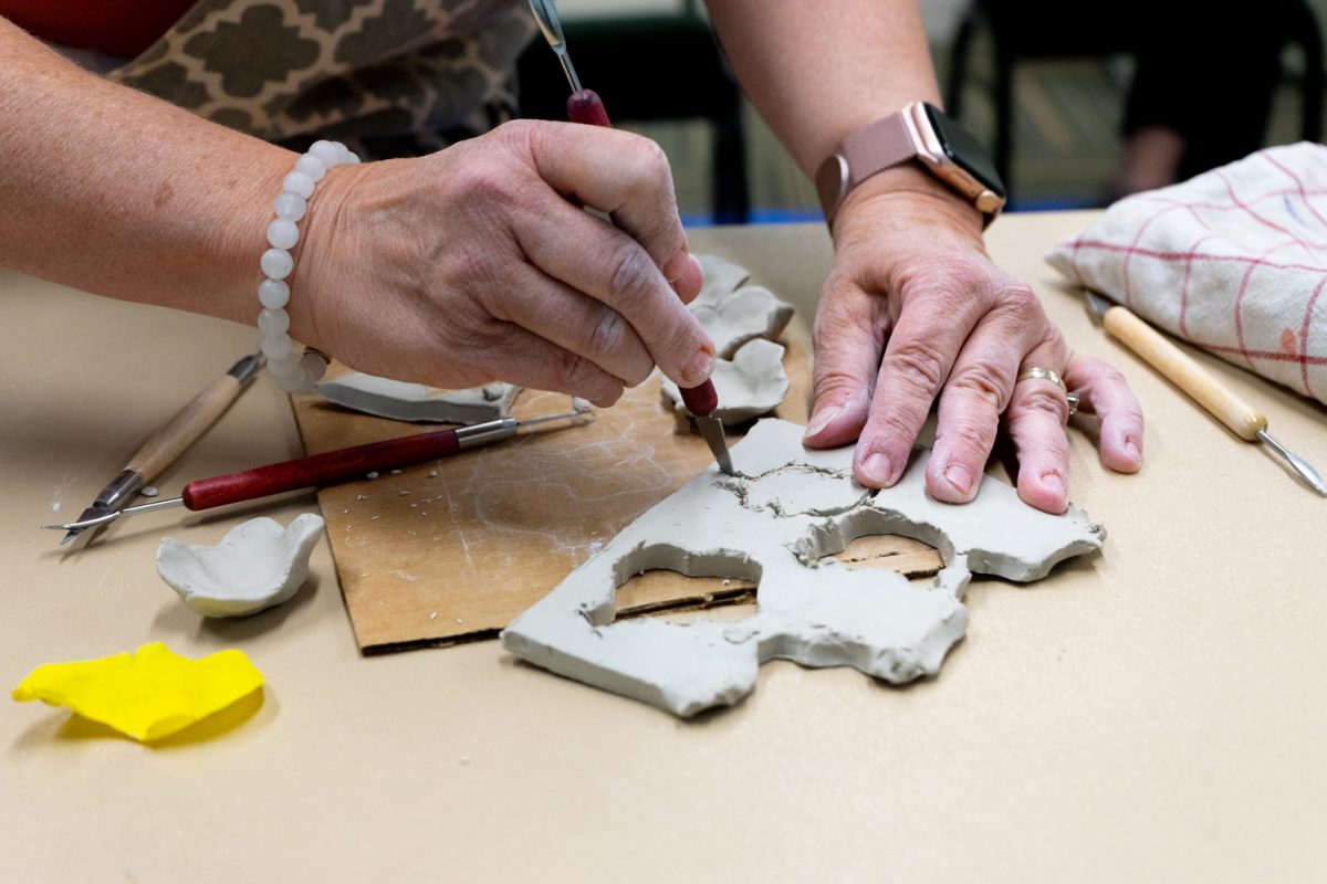 A person carves out clay to form a tree petal.