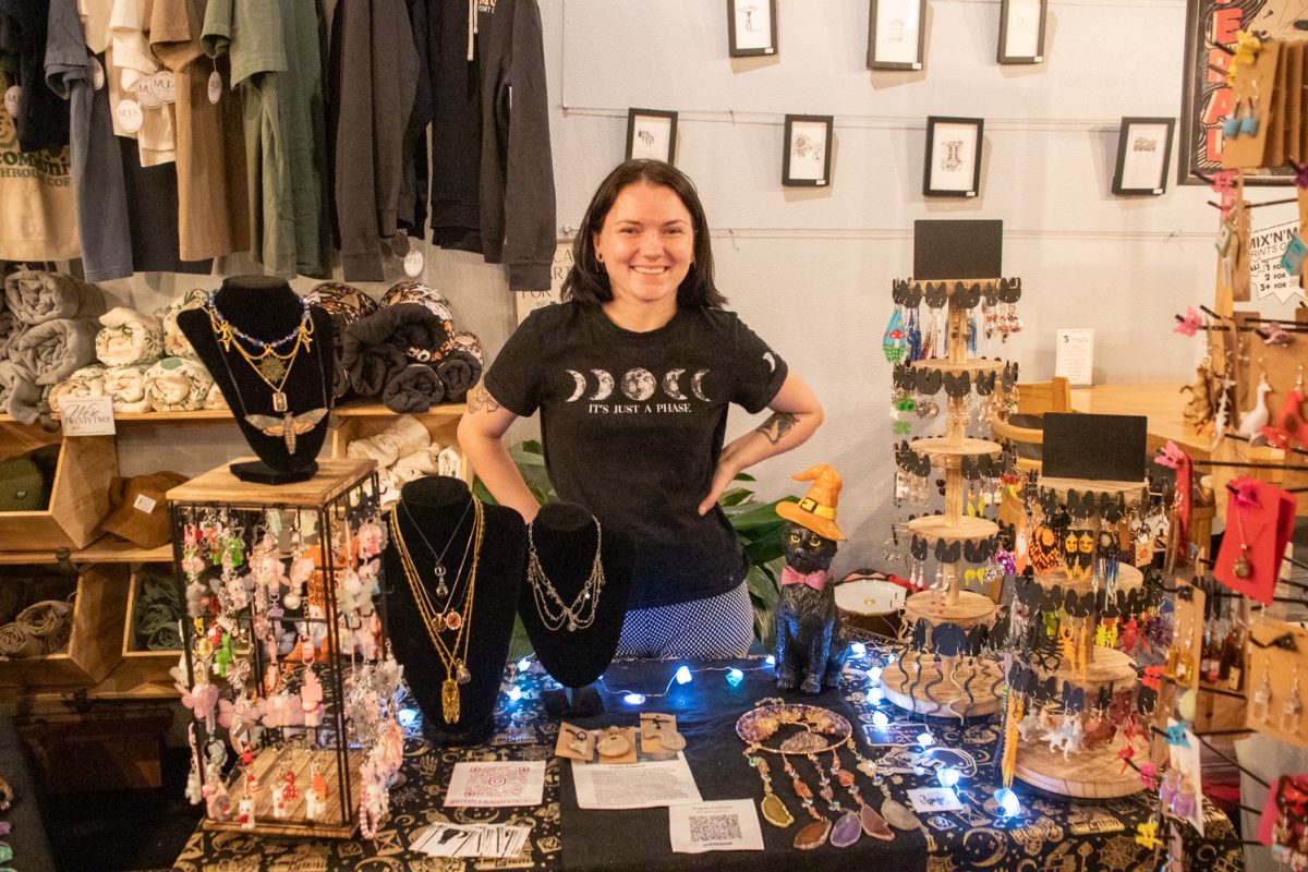 A person standing behind a table with earrings, keychains, and more for sale.