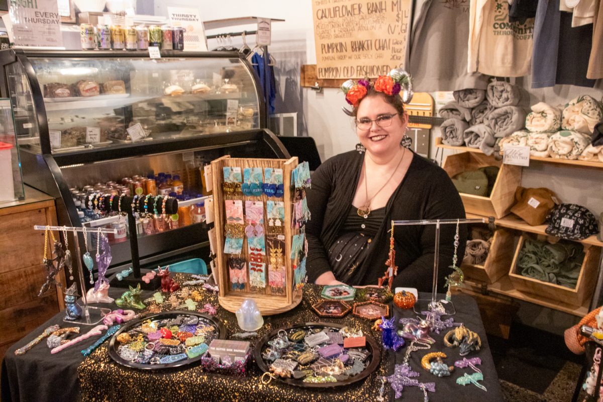 A person sitting behind a table with earrings, keychains, and more for sale.