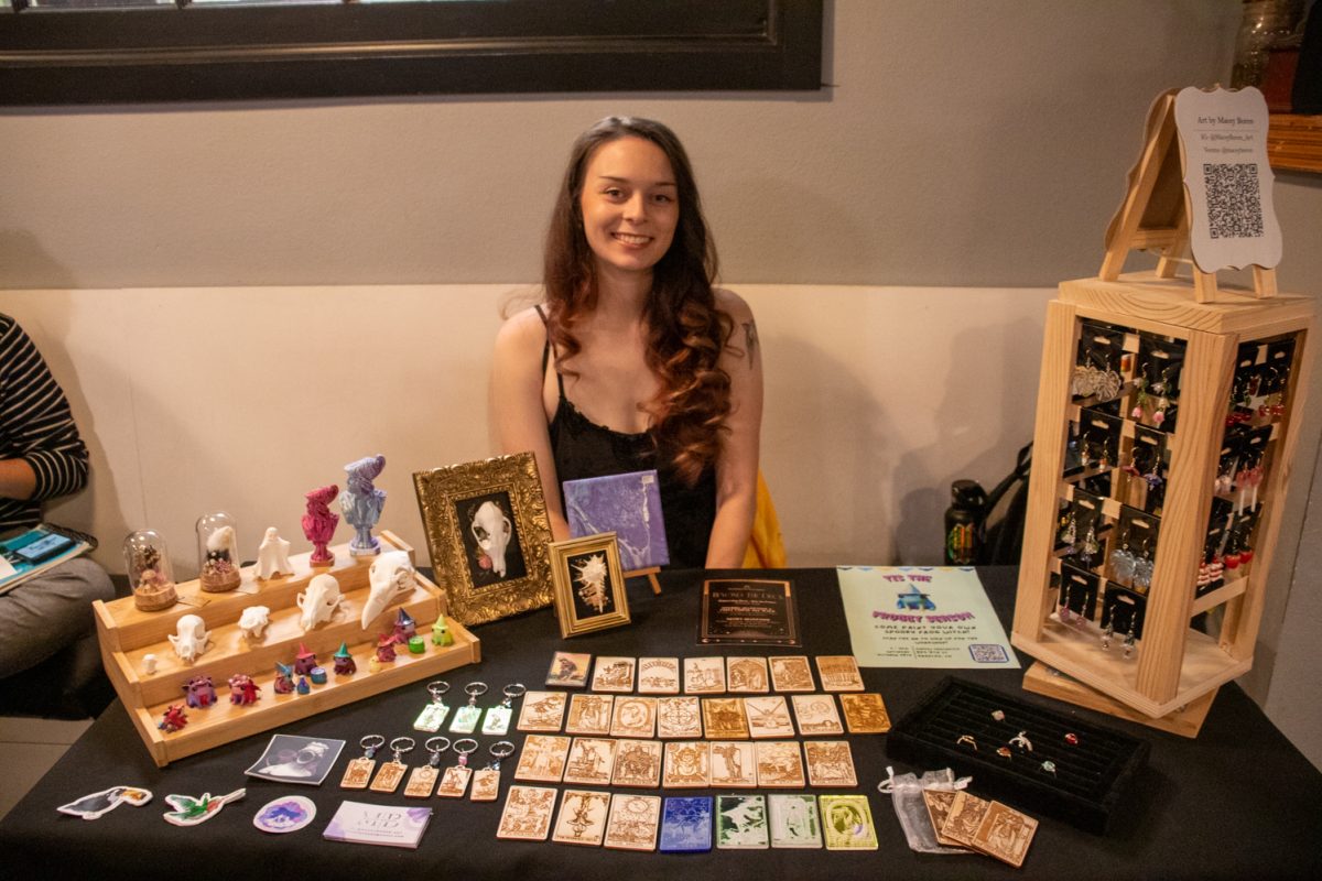 A person sitting behind a table with trinkets, earrings, and more for sale.