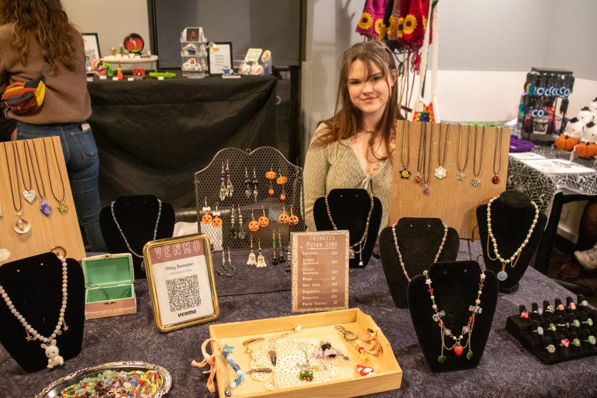 A person sitting behind a table with jewelry and trinkets for sale.