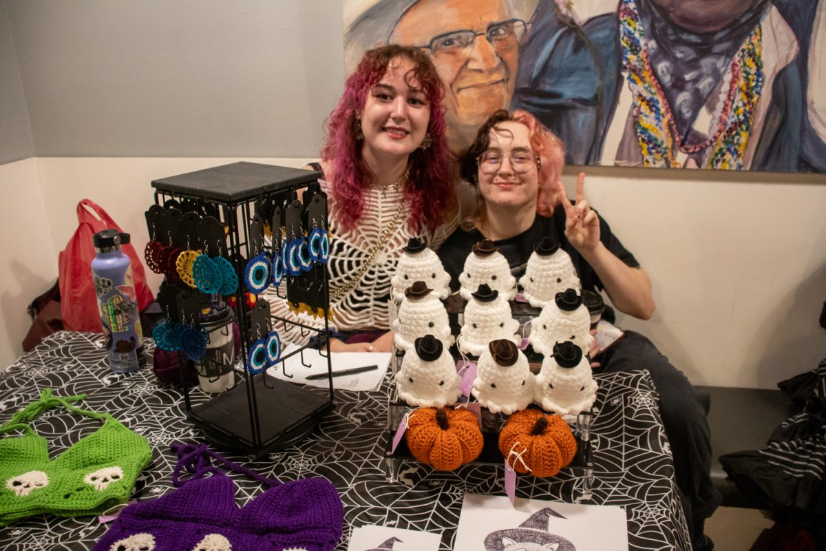 Two people sitting behind a table with crocheted objects for sale.