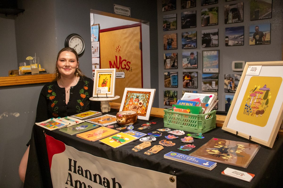 A person sitting next to a table with cards, keychains, stickers, and prints for sale.