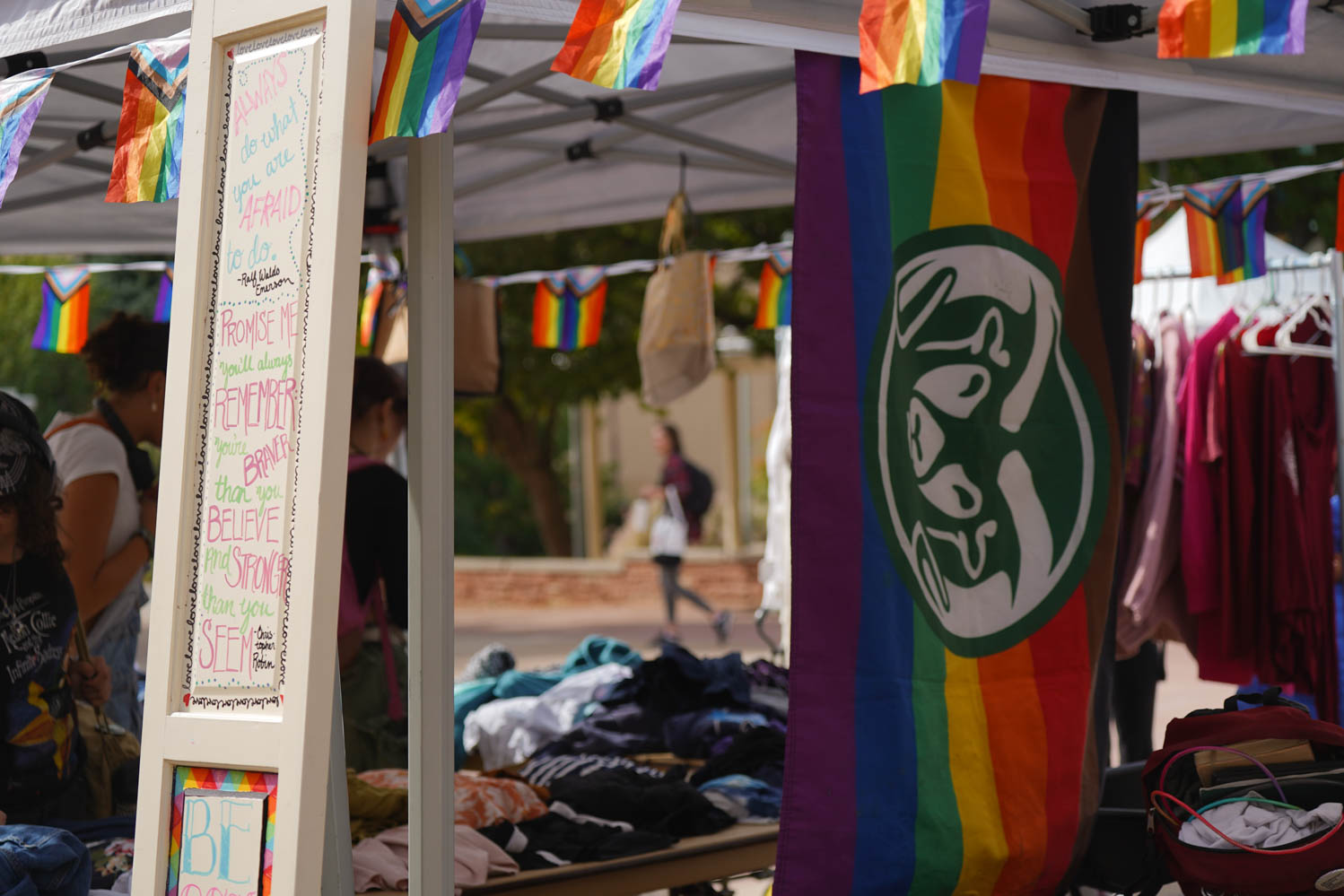 A door with quotes of affirmations on it rests on a tent with people under it. The tent has pride flags lining it.