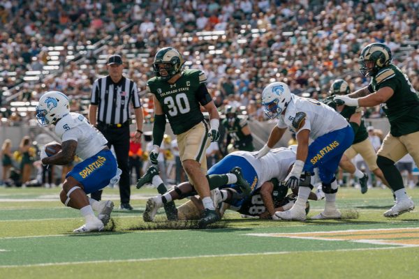 A football player with the ball runs from an opponent while another player is tackled to the ground.