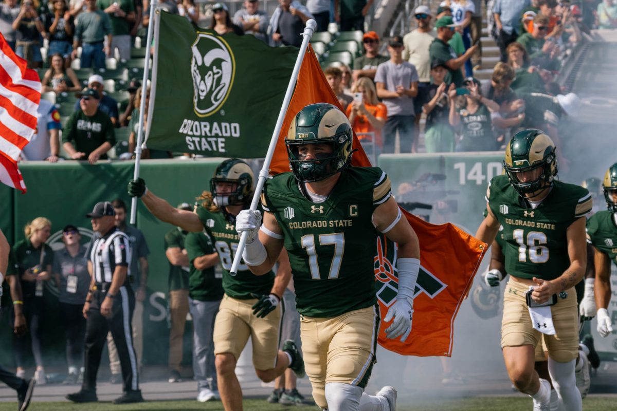 A football player carrying a flag runs out onto a field surrounded by other players.