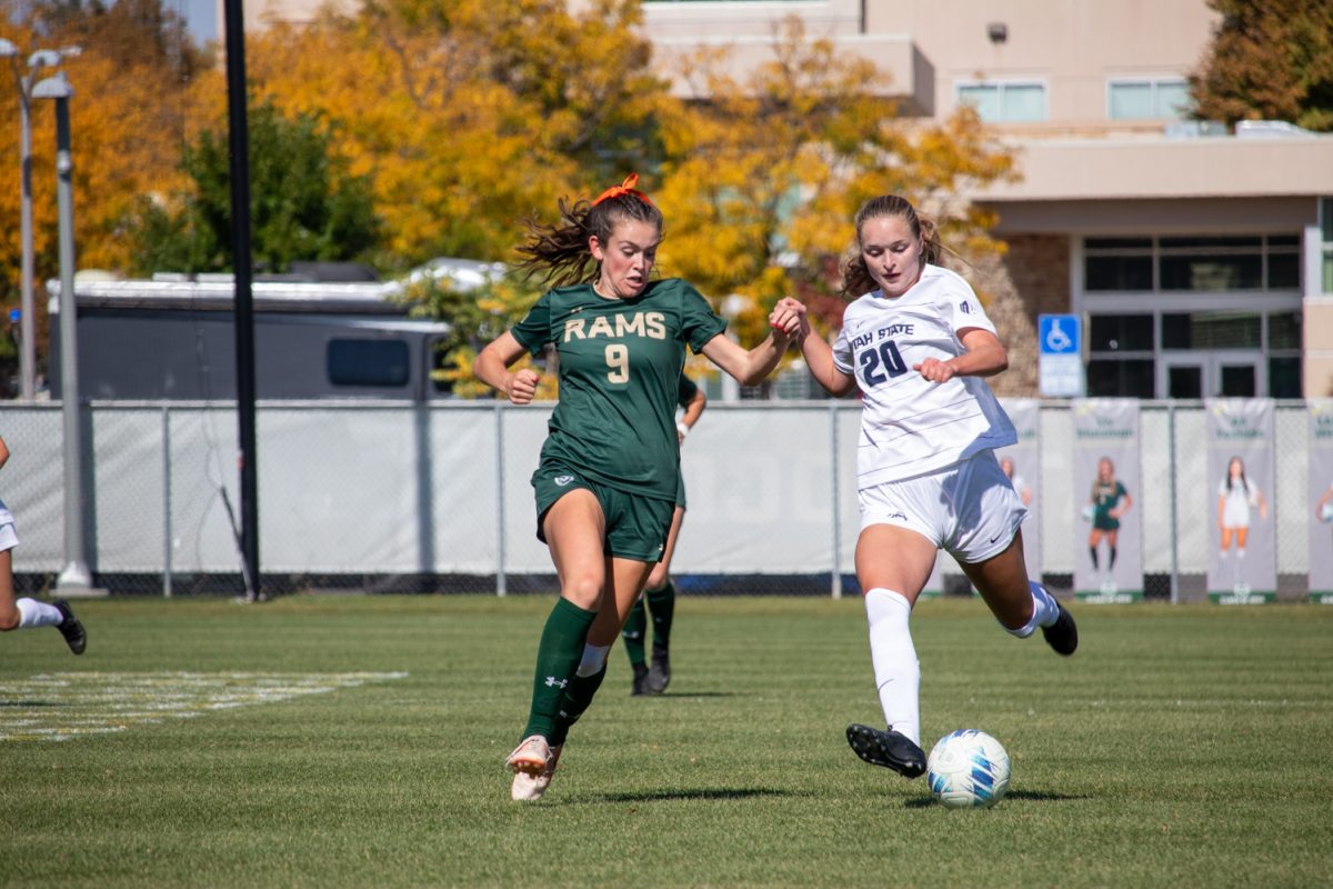 Two people chasing after a soccer ball.