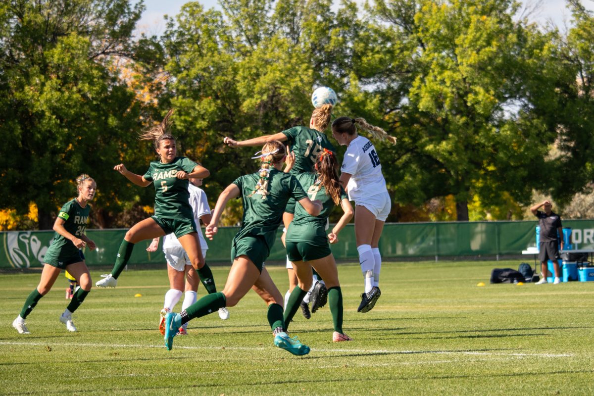 Multiple soccer players jump trying to get the ball.
