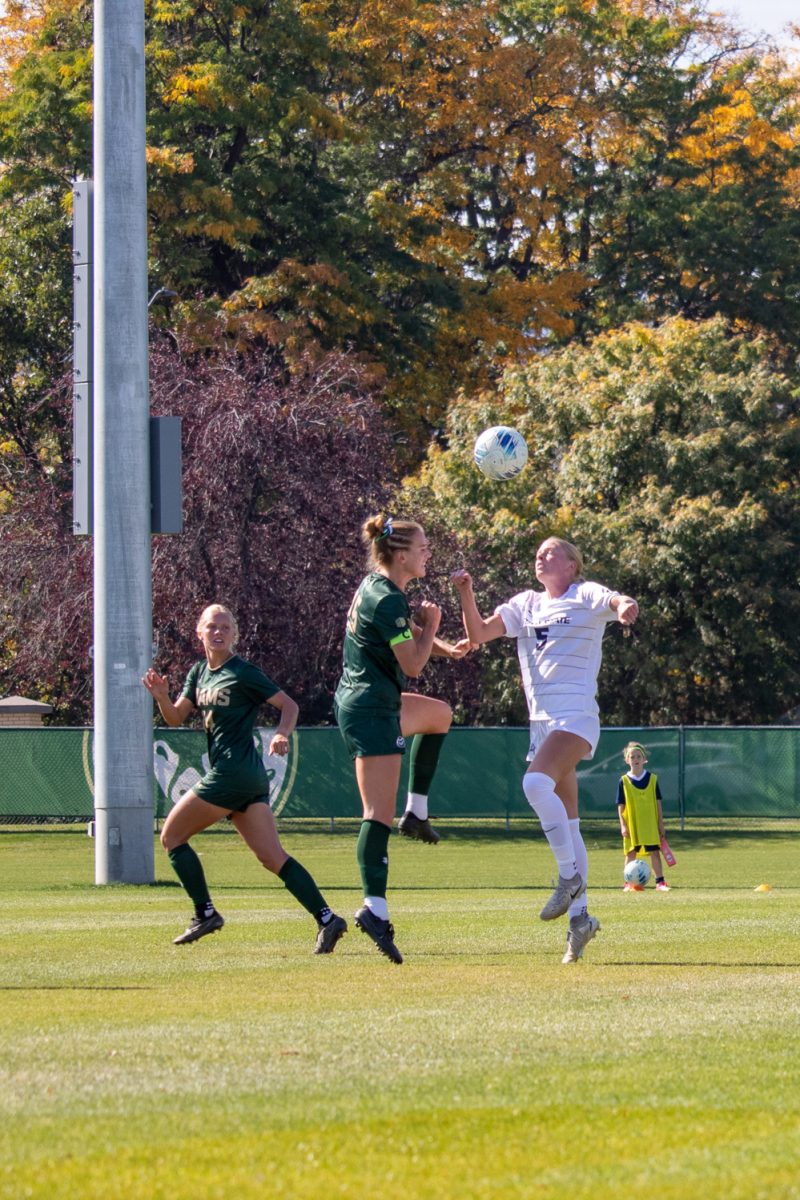Two people jumping in the air to hit a soccer ball on their heads.