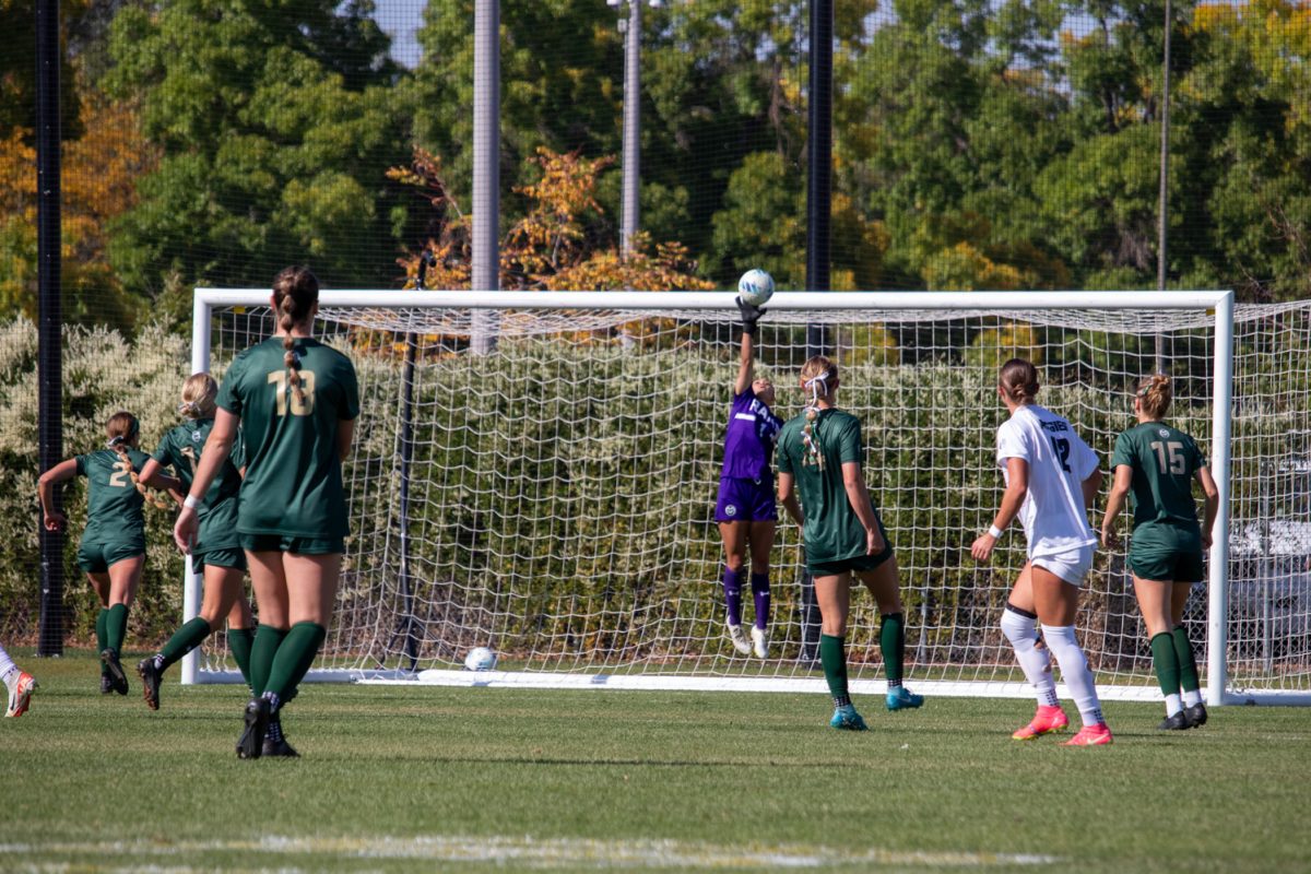A goalie jumping and stretching into the air to block a shot during a soccer game.