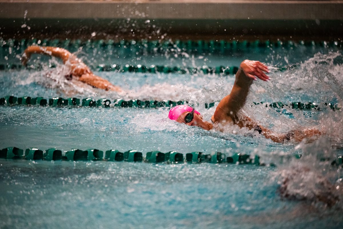 A swimmer in a pink swim cap and goggles comes up for air while swimming freestyle.