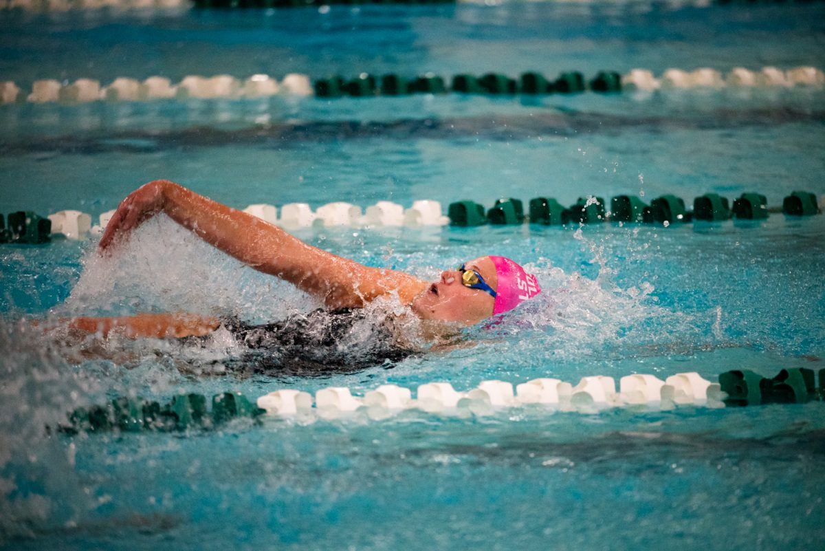 A swimmer in a pink cap and goggles takes a deep breath while swimming backstroke.