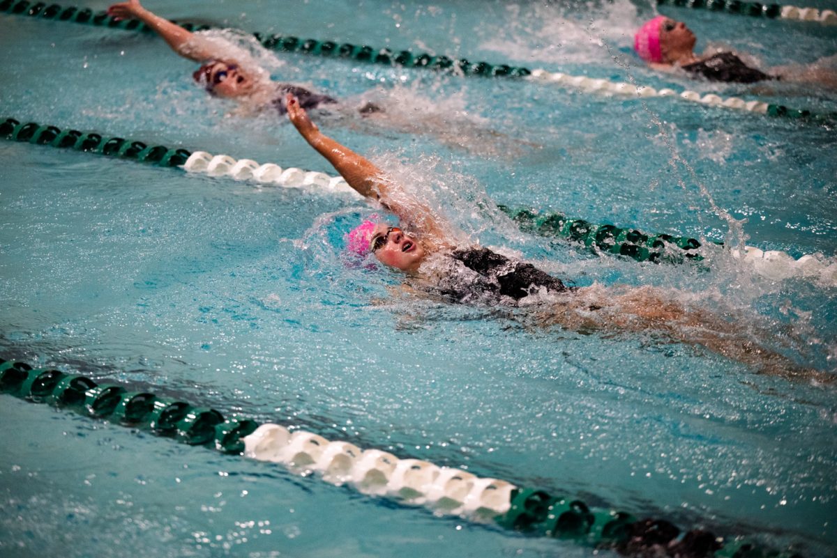 A swimmer in a pink cap and goggles takes a breath while swimming backstroke.