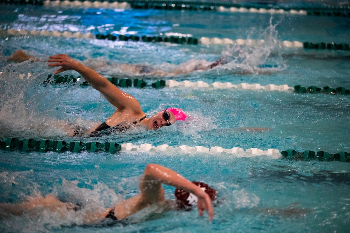 A swimmer in a pink cap and goggles comes up for air while swimming freestyle.