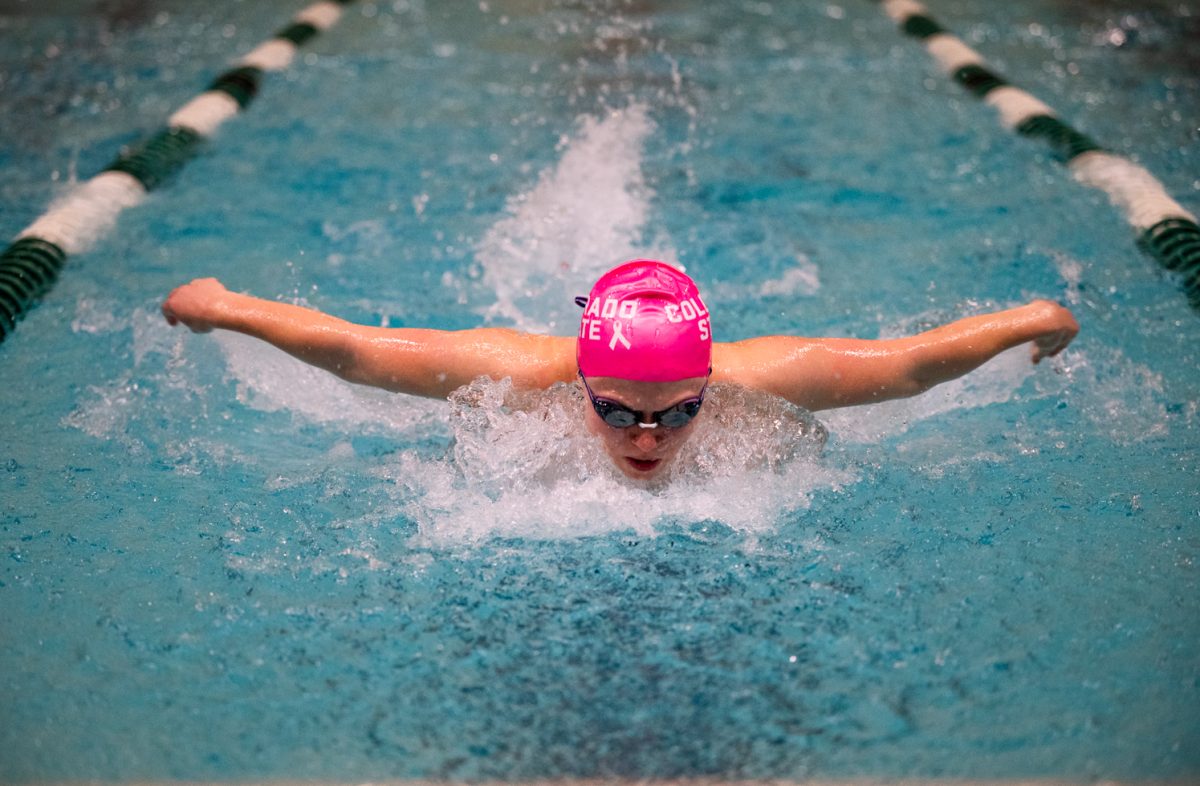 A swimmer in a pink cap and goggles comes up for air while swimming butterfly.