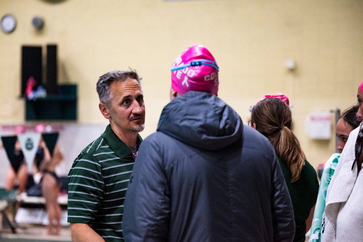 A man in a green and white striped shirt talks to a swimmer in a puffy jacket.