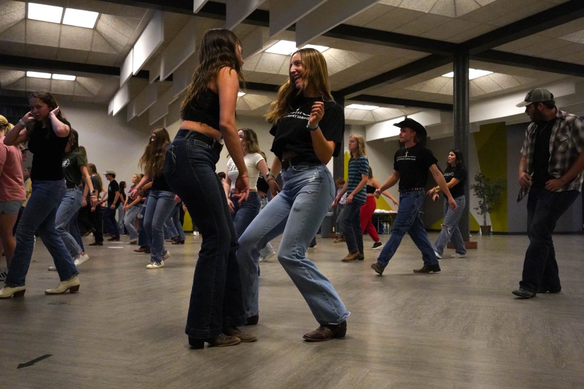 Two women dance in a group of people line dancing.