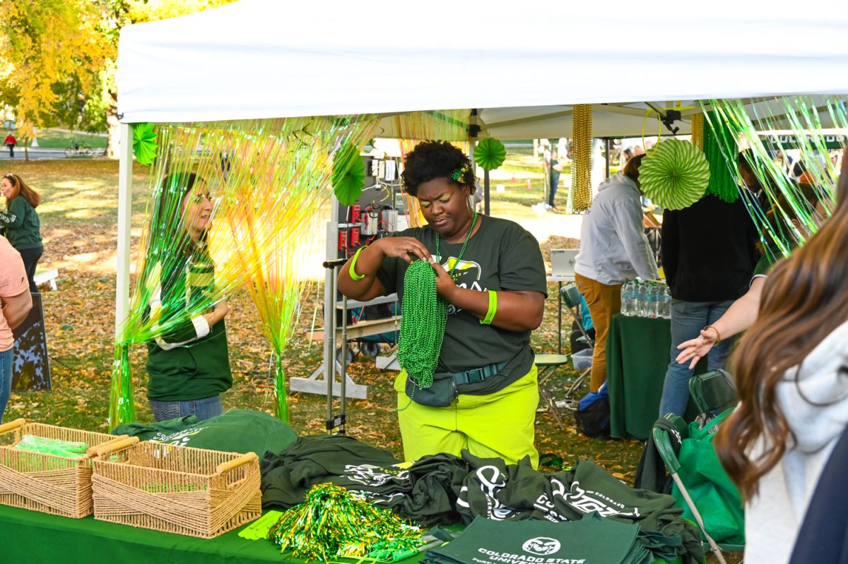 A woman examines a bundle of green necklaces, wearing all green and at a tent covered in green decorations and at a table with green CSU merch.